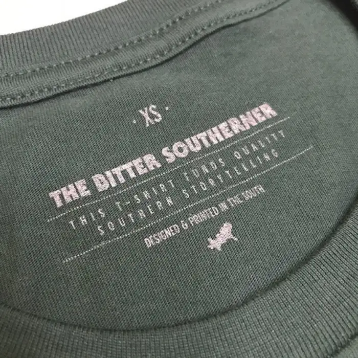 The same Bitter Southerner tag in the same 430 C gray ink on a green shirt