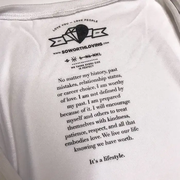 So Worth Loving printed neck tag in black ink on a white shirt, with the brand mission statement printed in full